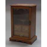 An Edwardian oak smoker's cabinet, with glazed door enclosing fitted interior and three drawers,