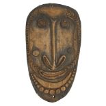 An oval tribal hardwood shield, 20th century, carved with a face within a beaded border, 95 x