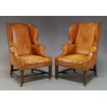 A pair of George III style wingback armchairs, mid 20th Century, with tan leather upholstery and