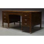 An oak desk, c.1930, the rounded rectangular top above an arrangement of seven drawers and two brush
