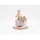 A Vienna porcelain figure in the form of a lady holding a posy, seated at a table with a flower