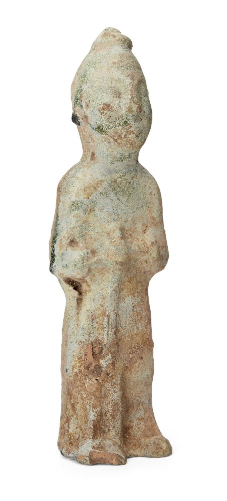 A Chinese pottery tomb figure, Han dynasty, modelled standing holding a rifle in front of his