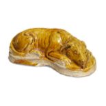 A Chinese pottery amber glazed dog, Tang dynasty, modelled in a recumbent pose with curved body, the