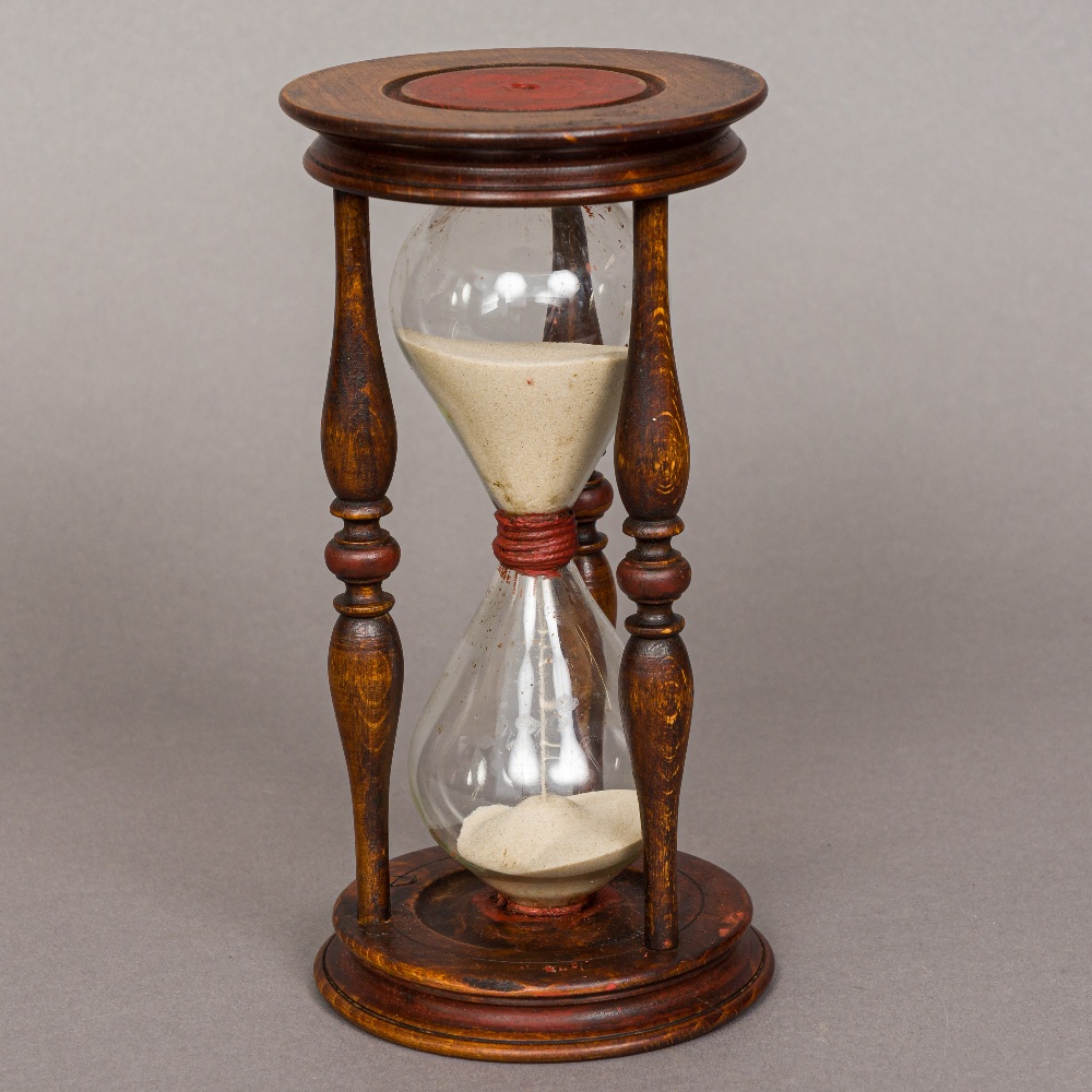 A carved wooden framed hourglass Of typical form, with red painted decoration to the top and bottom.