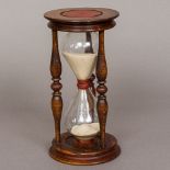 A carved wooden framed hourglass Of typical form, with red painted decoration to the top and bottom.