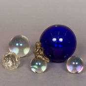 A collection of five glass balls Including a large cobalt blue example and another surmounted with