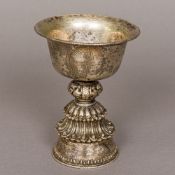 A Tibetan unmarked silver stem cup The engraved flared bowl above the central pierced knop,