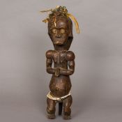 An African tribal carved wooden figure Modelled seated, hands clasped and with beadwork belt,