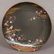 A 20th century Japanese porcelain dish Decorated with a bird on a blossoming branch on a black