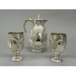 A silver jug and two silver goblets.