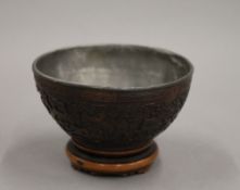 A 19th century Chinese carved coconut cup, mounted on a wooden stand. 7 cm high.