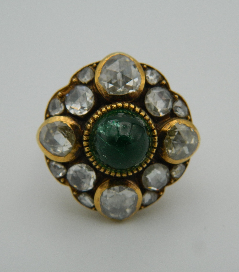 An unmarked 18 ct gold diamond and emerald ring. 2 cm diameter. Ring size I/J.