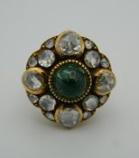 An unmarked 18 ct gold diamond and emerald ring. 2 cm diameter. Ring size I/J.