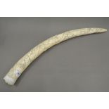 An early 20th century carved tusk, worked in the round with figures and animals. 56.5 cm long.