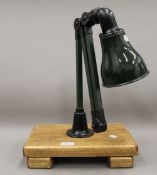 A green painted and enamel hinged machinists lamp mounted on a wooden stand. The stand 33 cm wide.