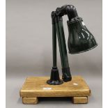 A green painted and enamel hinged machinists lamp mounted on a wooden stand. The stand 33 cm wide.