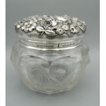 A finely cut glass jar with heavily worked sterling silver lid extensively worked with flowers and