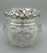 A finely cut glass jar with heavily worked sterling silver lid extensively worked with flowers and