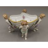 A porcelain table centrepiece bowl supported by four cherubs. 34 cm wide.