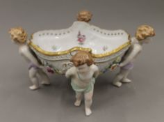 A porcelain table centrepiece bowl supported by four cherubs. 34 cm wide.