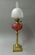 A Victorian oil lamp with cranberry glass reservoir. 76 cm high.