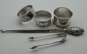 Three silver napkin rings, a pair of silver tongs and a button hook. 67.