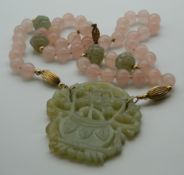 A carved jade pendant on a carved jade and rose quartz necklace. The pendant 6 cm wide.