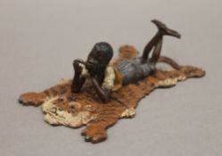 A cold painted bronze model of a boy on a tiger rug. 12 cm long.