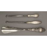 A silver handled shoehorn and two silver handled button hooks. The former 22 cm long.