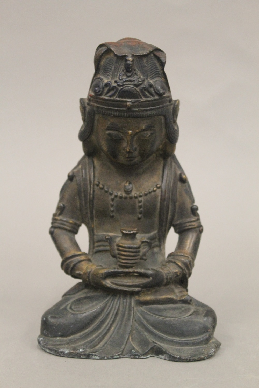 A seated bronze deity holding a teapot. 18 cm high.