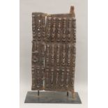 A carved wooden tribal Dogon door, on a display stand. 66.5 cm high.