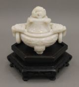 A Chinese carved white jade lidded censer, on a carved hardwood stand. The censer 10 cm high.