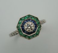 An Art Deco style platinum, emerald, sapphire and diamond ring with diamond set shoulders.