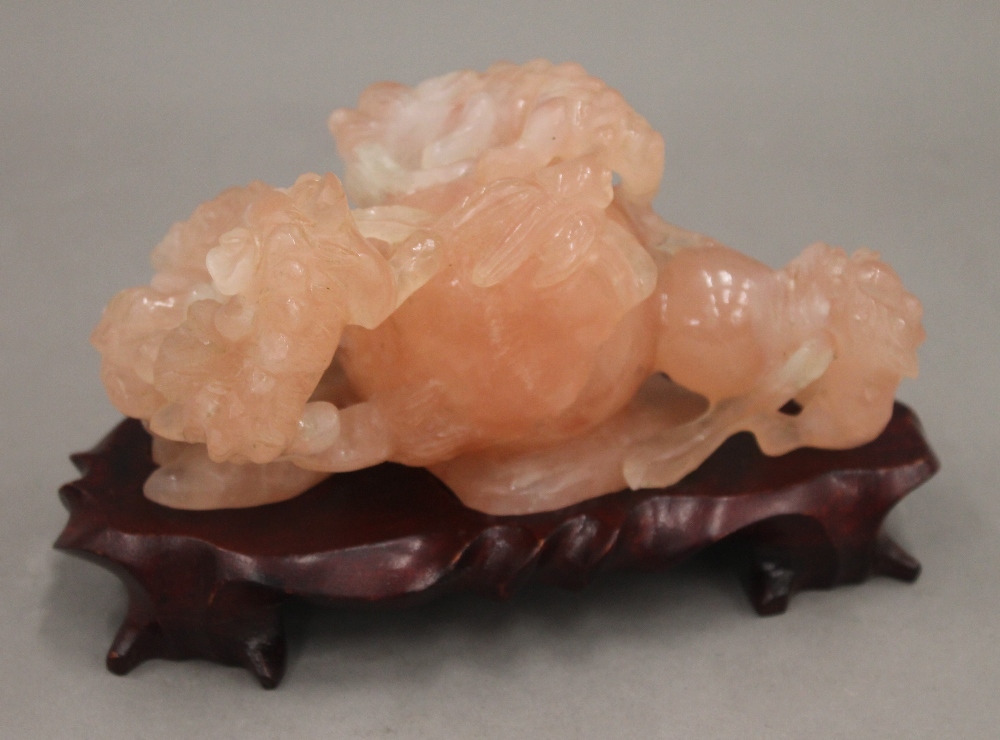 A Chinese carved rose quartz group formed as dogs-of-fo, on a carved wooden stand.