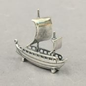 A silver model of a boat. 4 cm long.