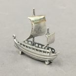 A silver model of a boat. 4 cm long.