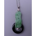 An Art Deco carved apple green jade, onyx and diamond pendant, set in platinum, on a platinum chain.