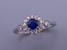 An 18 ct white gold sapphire and diamond cluster ring with diamond shoulders. Ring size M. 2.