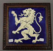 A porcelain tile depicting a rampant lion, set in an oak frame. 28 cm wide.