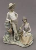 A Lladro porcelain group formed as a young shepherd and shepherdess feeding a lamb. 27 cm high.