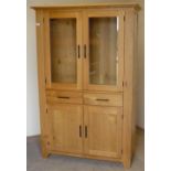 Modern light wood cabinet with two upper glazed doors above two drawers and two panelled doors (