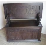 Oak monks bench, tilt top with carved shield, with lion arm supports and linen fold front, lift up