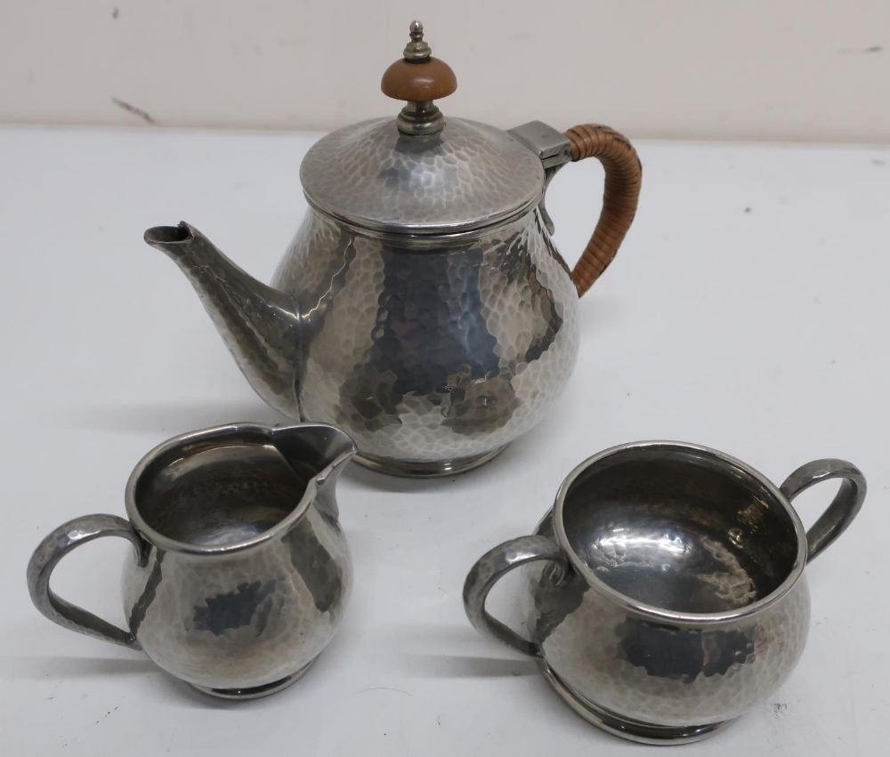 Tudric hammered pewter bachelors three piece tea service, the tea pot with wicker bound handle and