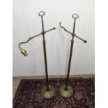 A pair of brass adjustable height and adjustable arm floor lamps on circular bases.