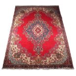 A Kerman woollen hand-made carpet with red ground, 122 by 88ins. (310 by 224cms.).