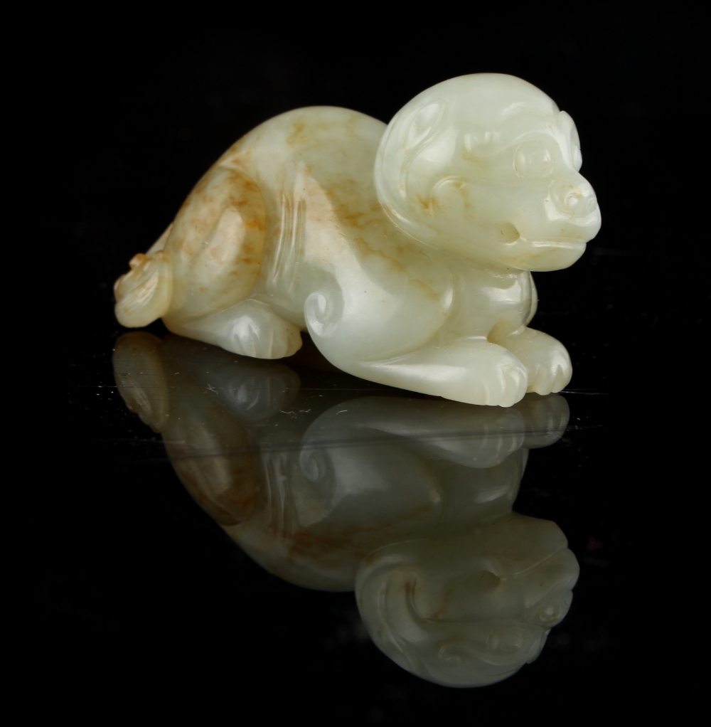 A Chinese carved pale celadon & russet jade model of a recumbent lion cub, 2.35ins. (6cms.) long.