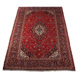 A Kashan woollen hand-made carpet with red ground, 111 by 79ins. (282 by 201cms.).