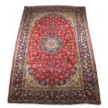 A Kashan woollen hand-made carpet with red ground, 151 by 99ins. (384 by 250cms.).