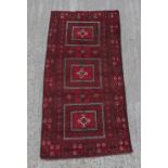 A Belouch woollen hand-made rug with burgundy ground, 89 by 43ins. (227 by 110cms.).