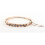 An unmarked yellow gold sapphire & diamond hinged bangle, the nine sapphires weighing a total of